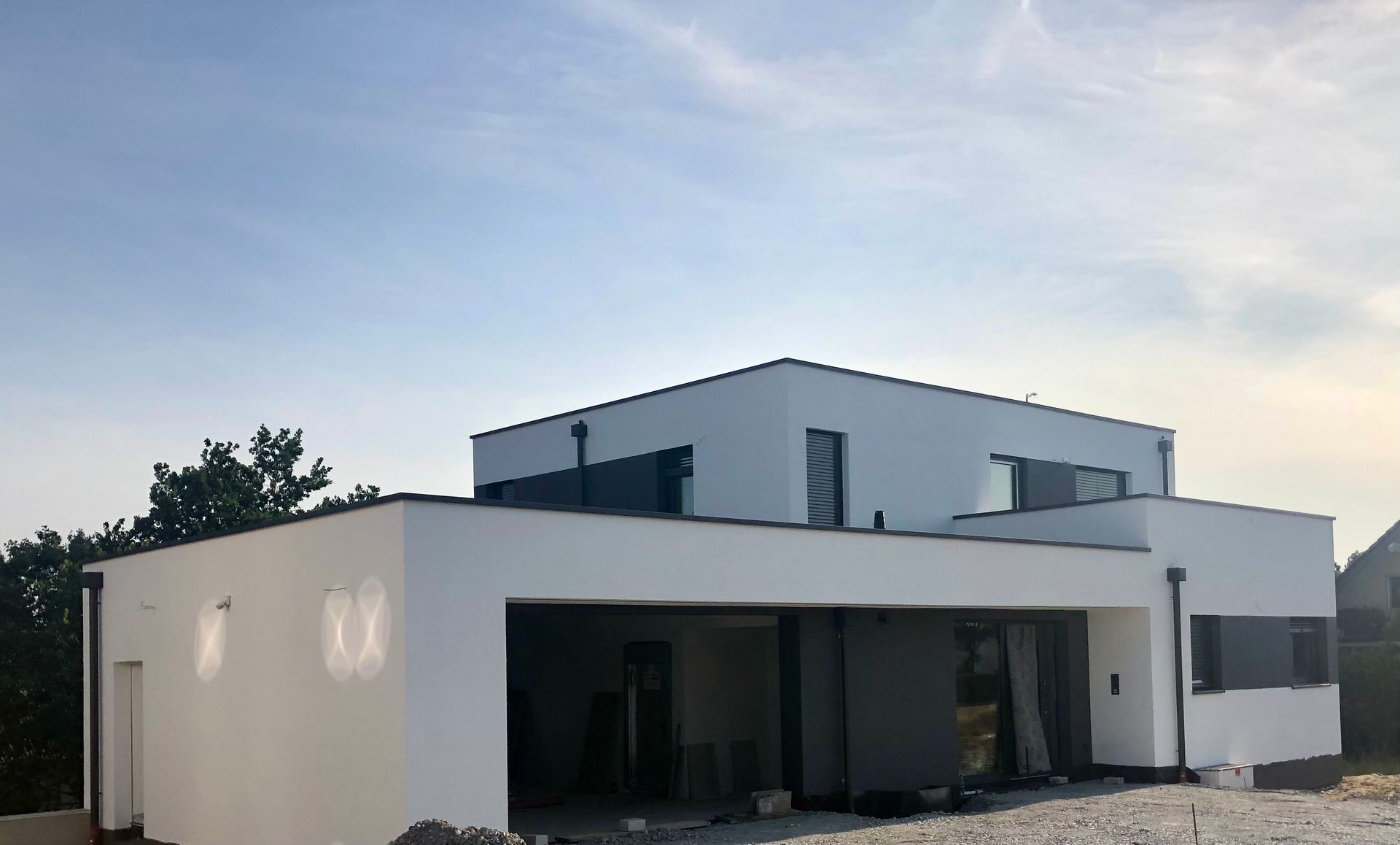 Ein modernes, weißes, zweistöckiges Haus mit Flachdach und dunklen Fensterrahmen unter einem klaren blauen Himmel.