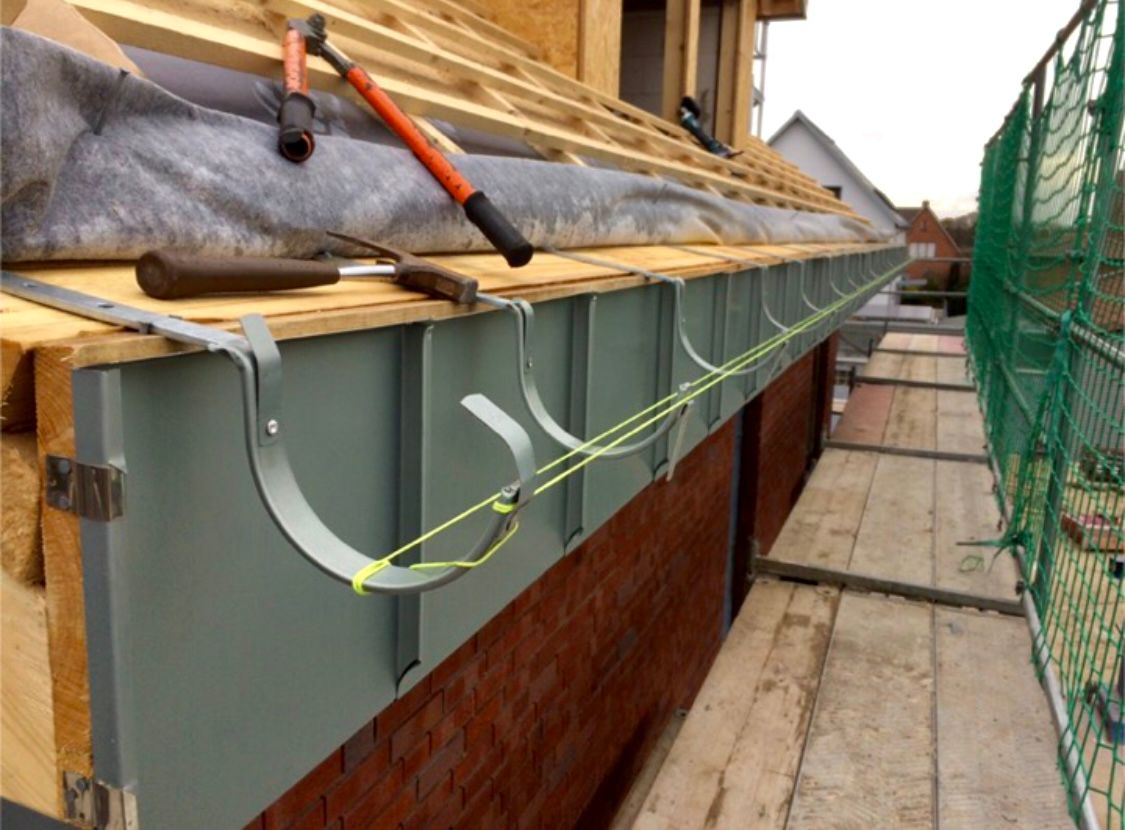 Metallene Dachrinnenhalterungen sind an einer Dachkante eines im Bau befindlichen Gebäudes angebracht