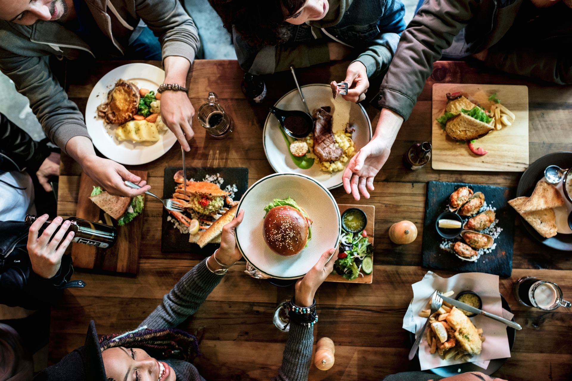 Des personnes se servent à une table garnie de plats variés, notamment des hamburgers, du poulet et des accompagnements.