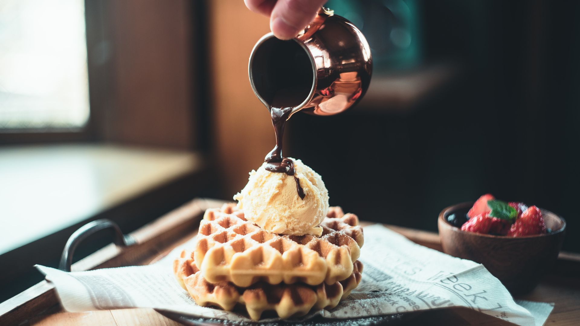 Gaufres garnies de glace, arrosées de sauce au chocolat, servies sur un plateau en bois avec des fruits rouges.