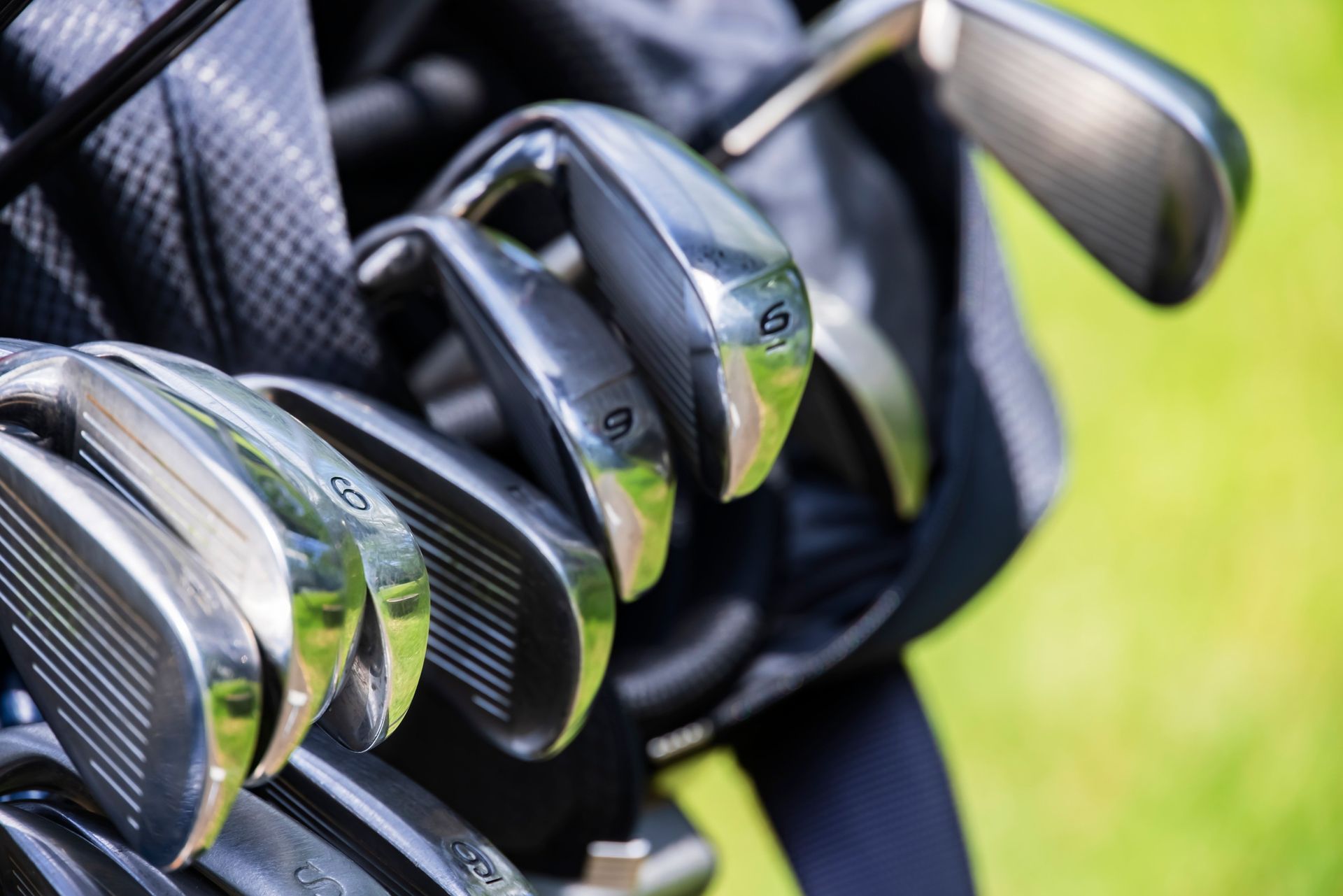 Primer plano de una bolsa de golf con varios hierros de golf de metal brillante visibles, sobre un fondo verde y herboso.