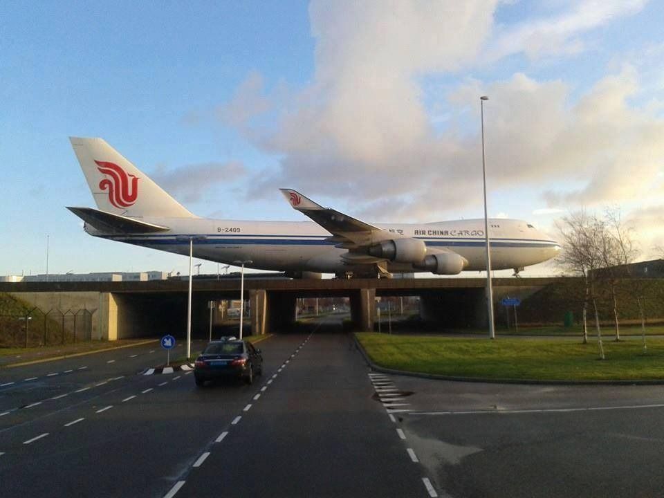 Un gran Boeing 747 de Air China está estacionado en un puente sobre una carretera, con un automóvil circulando debajo.