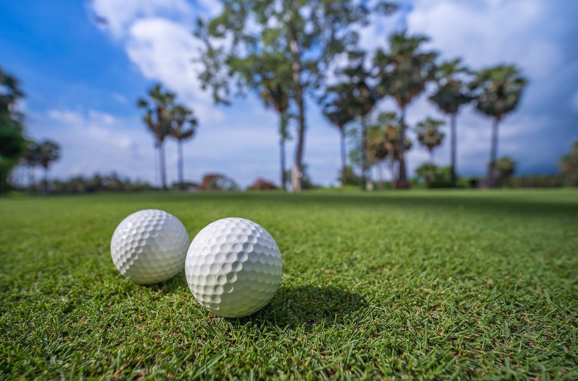 Dos pelotas de golf blancas sobre césped verde, con un campo de golf y un cielo azul de fondo.