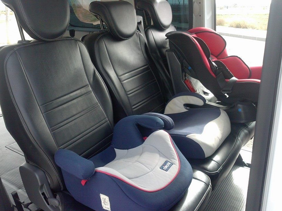 Asiento trasero de un vehículo con tres sillas infantiles, incluyendo elevadores rojos y azules. Los asientos son de cuero negro.