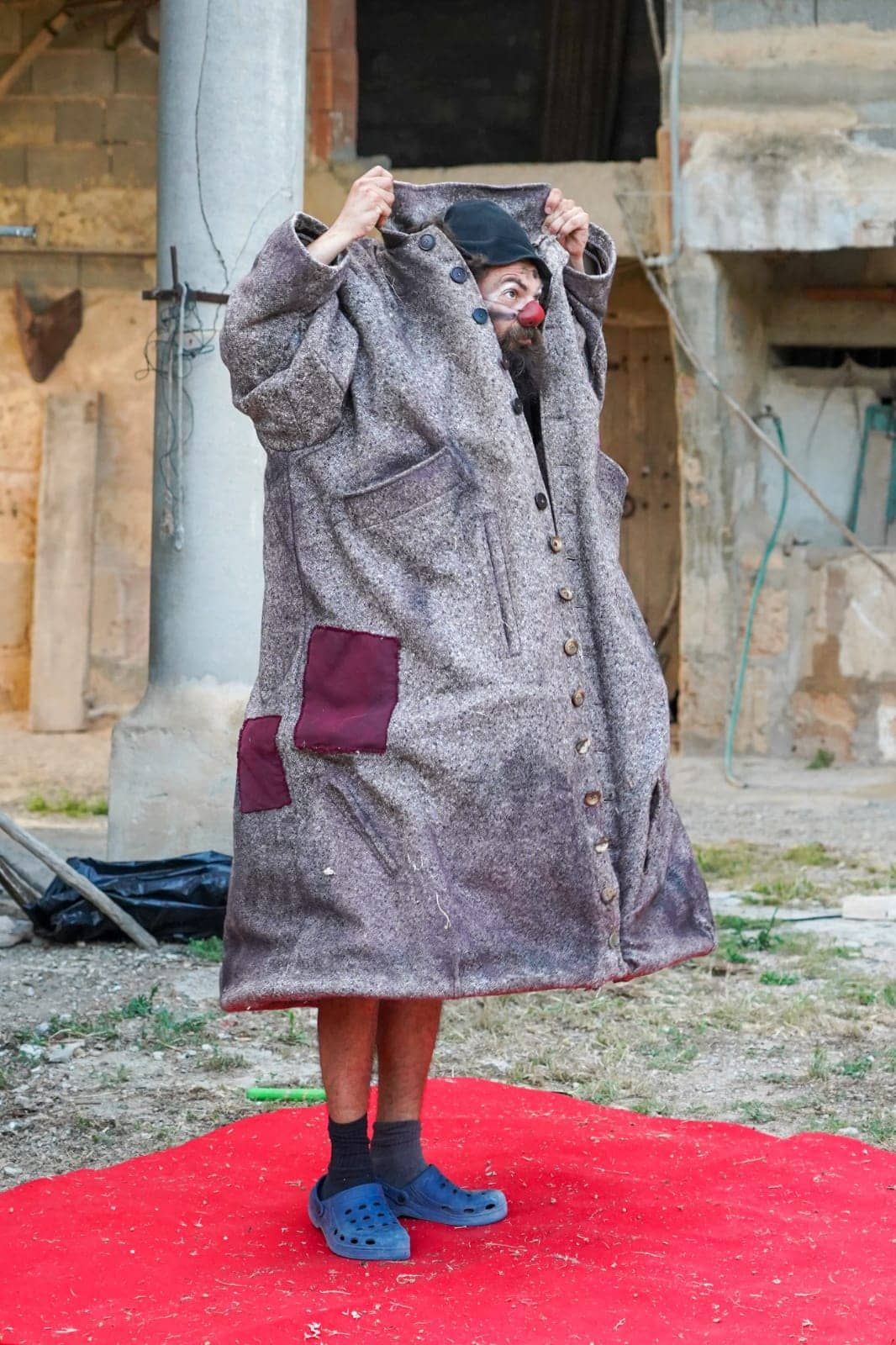 Una persona está parada sobre una alfombra roja sosteniendo un abrigo sobre su cabeza.