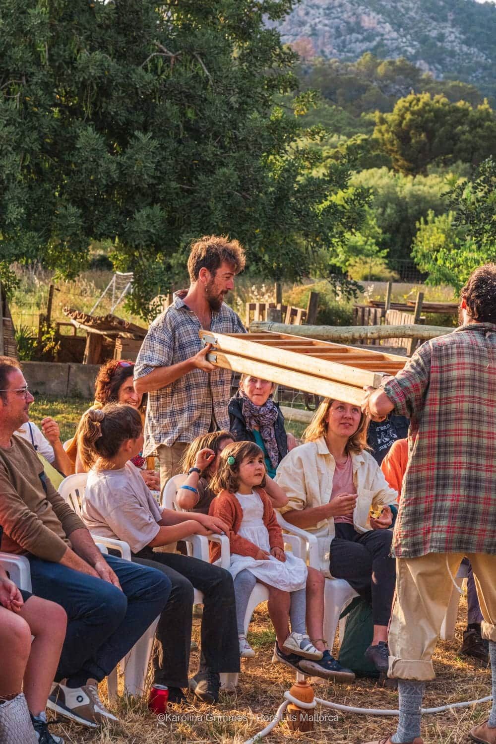 Un grupo de personas están sentadas en sillas y un hombre está parado frente a ellos sosteniendo una caja de madera.