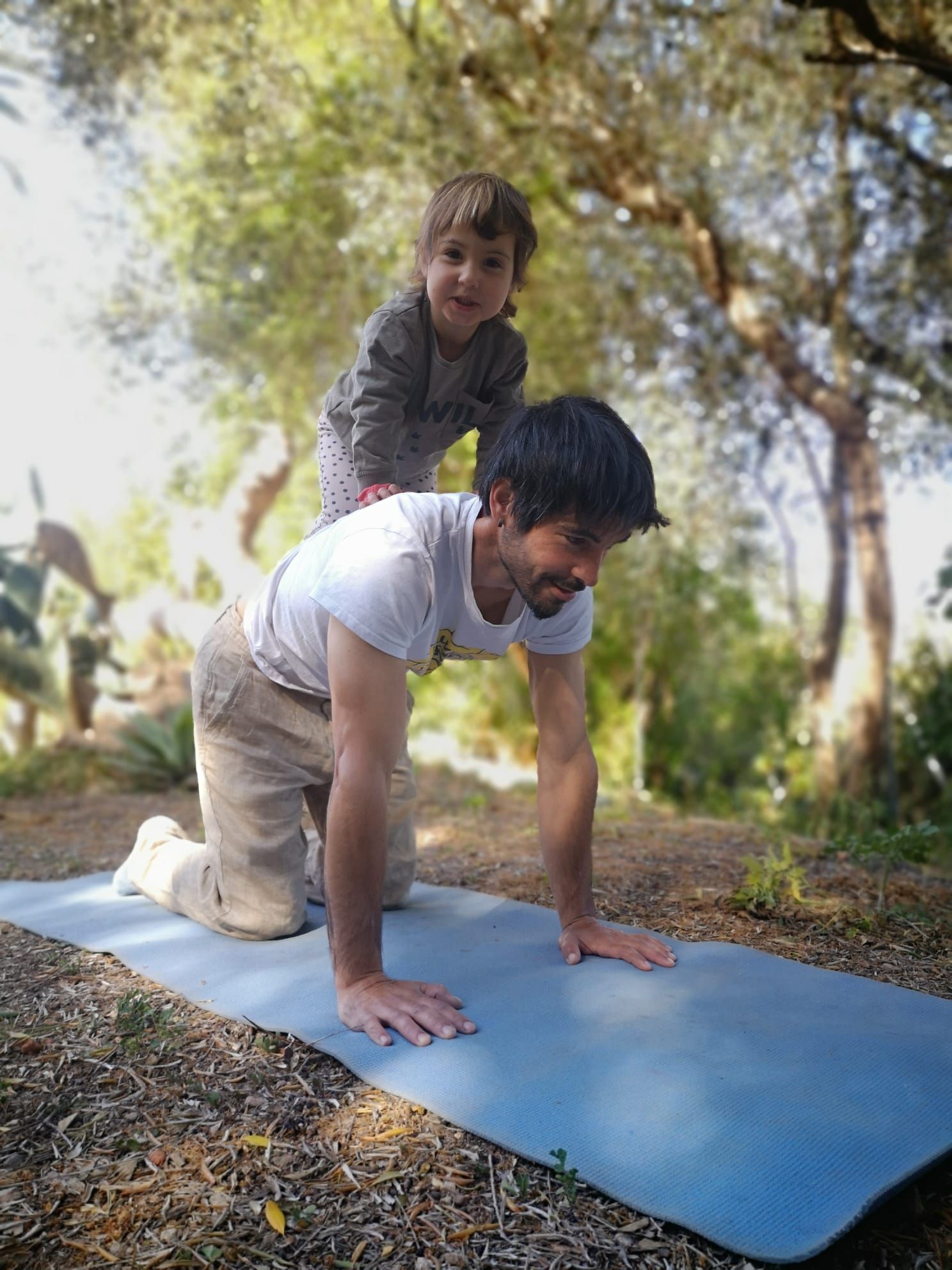 Un hombre está arrodillado sobre una esterilla de yoga con un niño en su espalda.