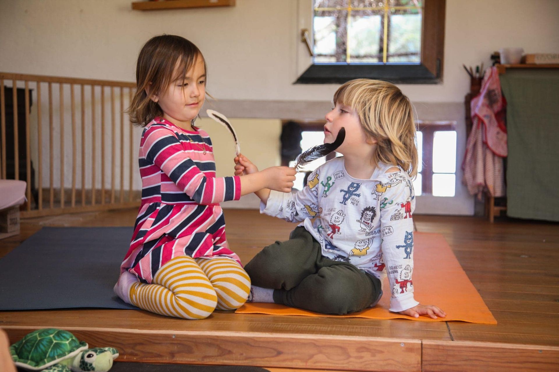 Un niño y una niña están sentados en una esterilla de yoga jugando con un juguete.