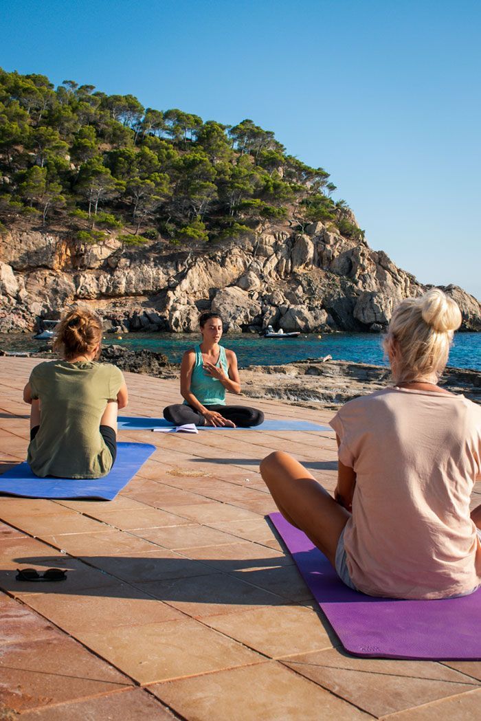 Un grupo de personas está sentada sobre colchonetas de yoga en la playa.