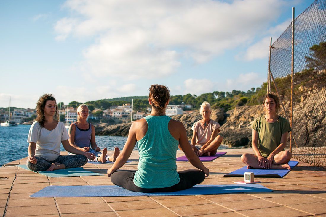 Un grupo de personas está sentada sobre colchonetas de yoga en un muelle.