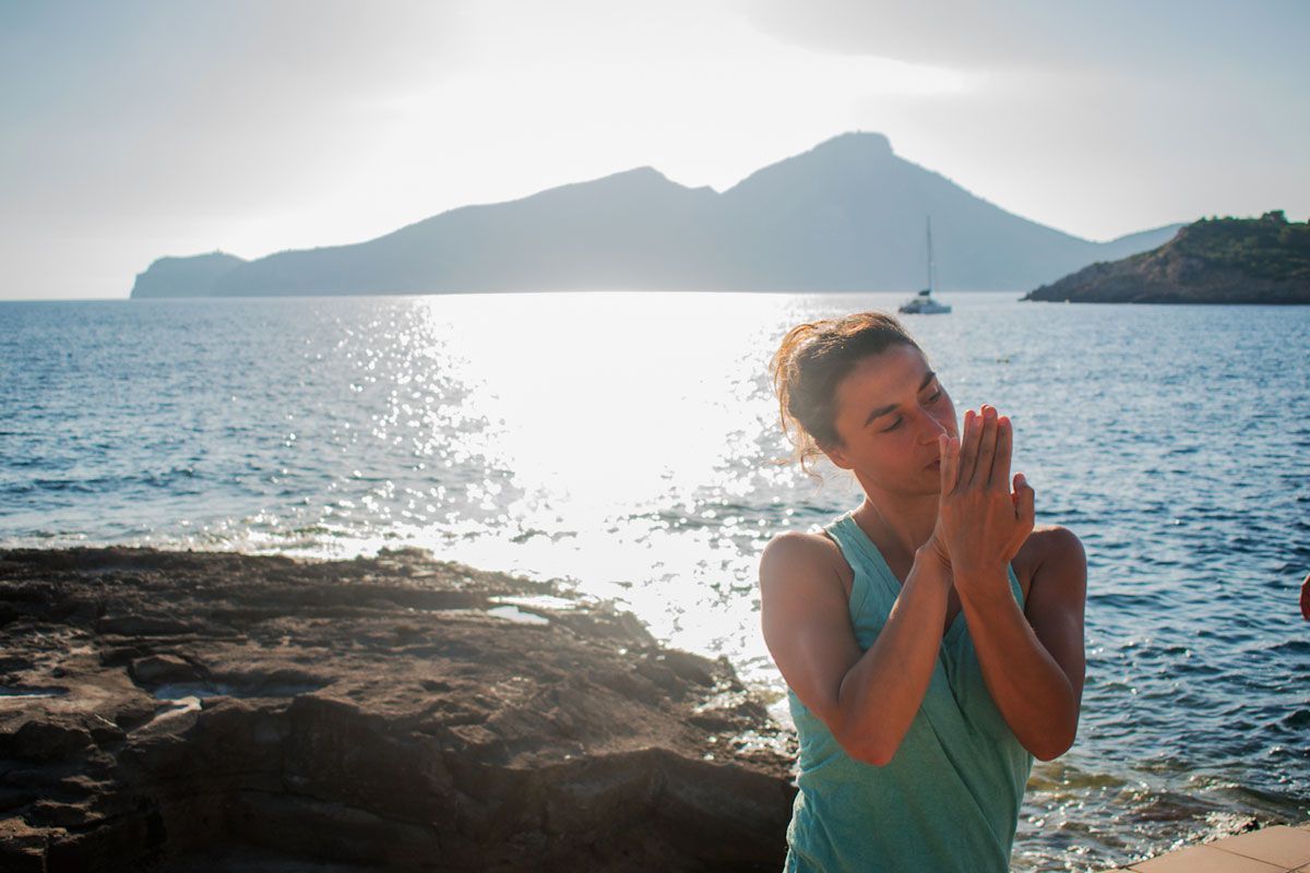 Una mujer está orando en la playa cerca del océano.