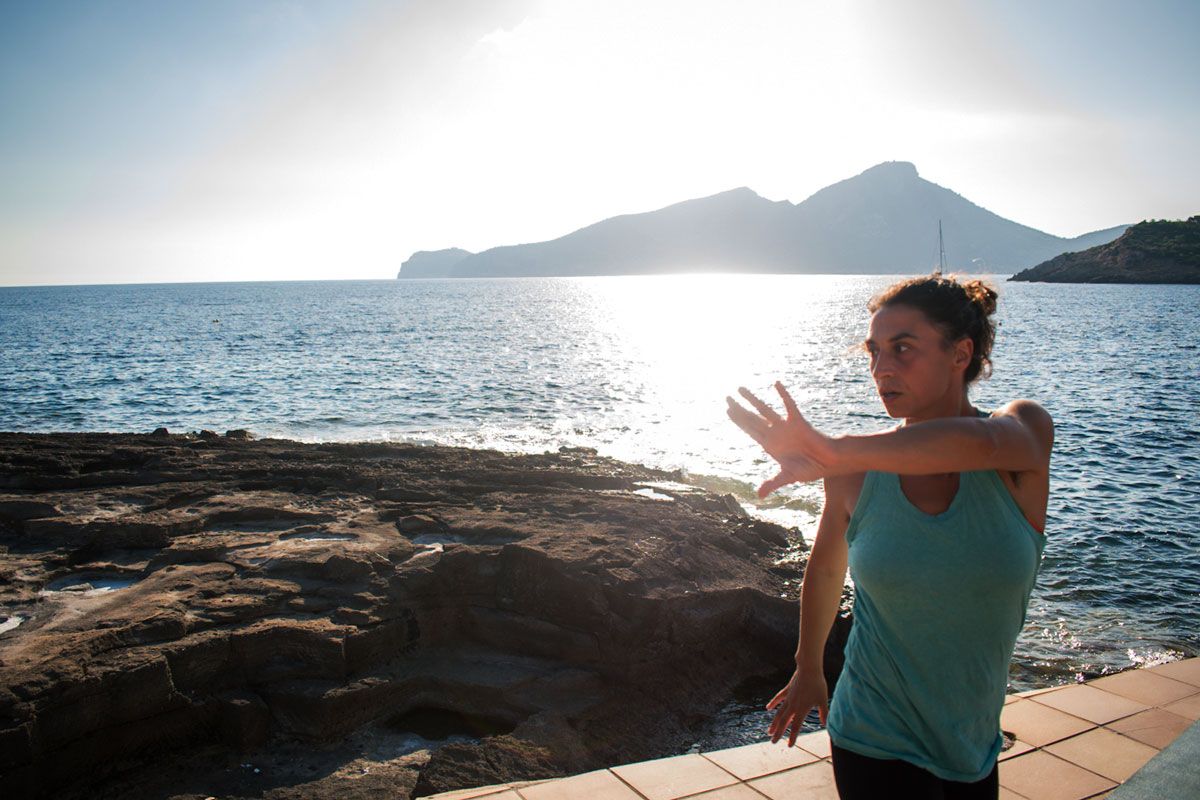 Una mujer estira los brazos frente al océano.