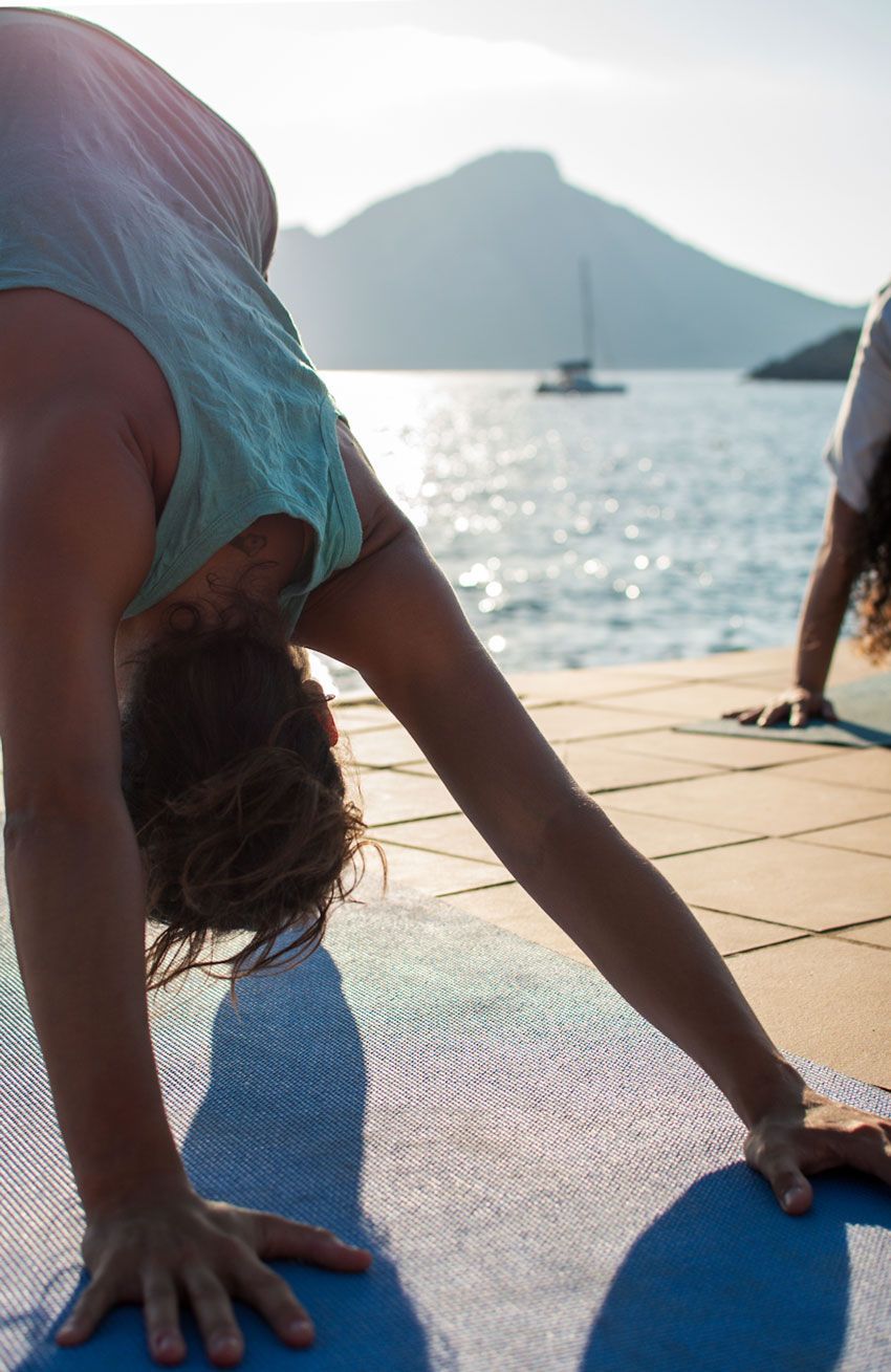 Una mujer está haciendo una pose de yoga en una colchoneta cerca del océano.