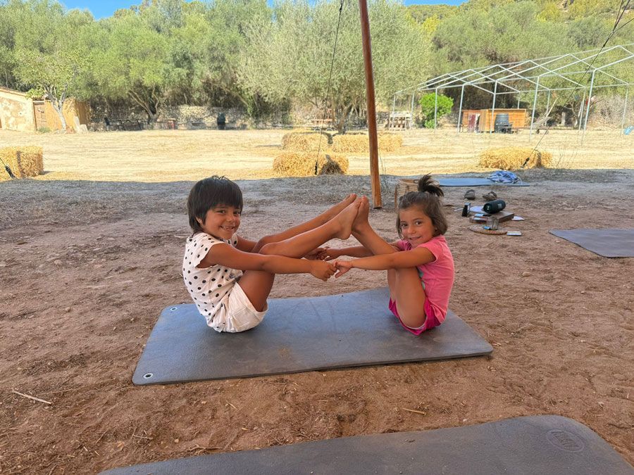 Dos chicas jóvenes están sentadas sobre colchonetas de yoga en el suelo.