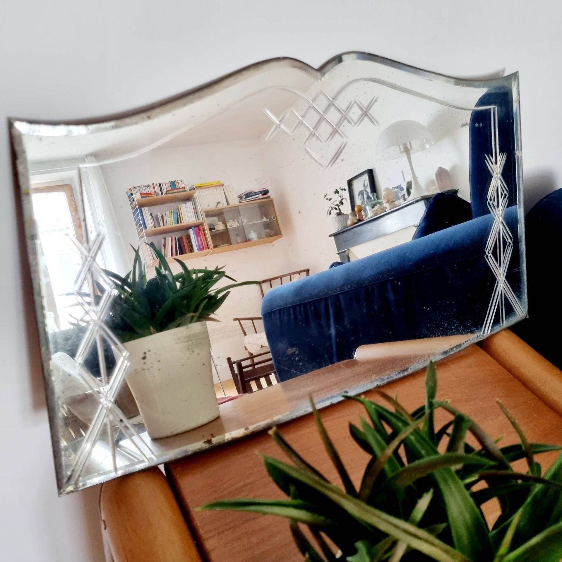 Miroir en forme de livre posé sur table reflétant un canapé bleu et une fausse plante verte