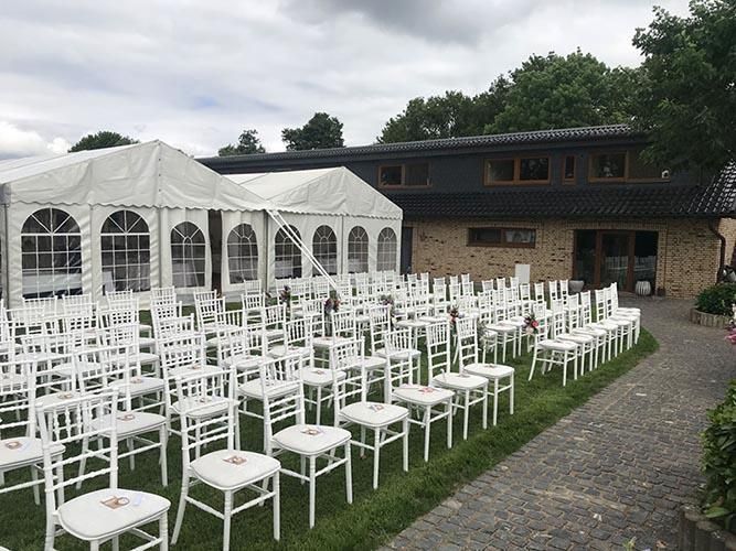 Vor einem Zelt steht eine Reihe weißer Stühle.