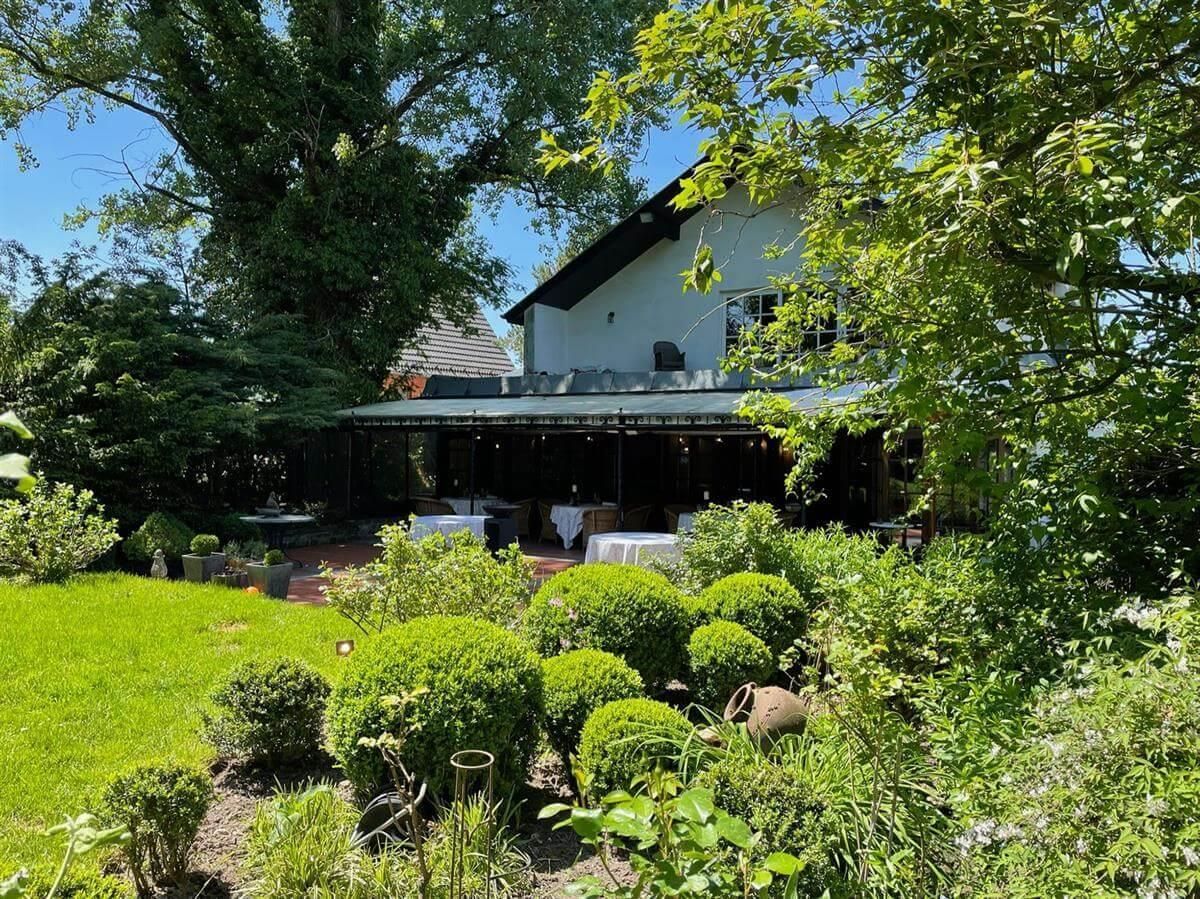 Ein großes weißes Haus ist von Bäumen und Büschen umgeben.