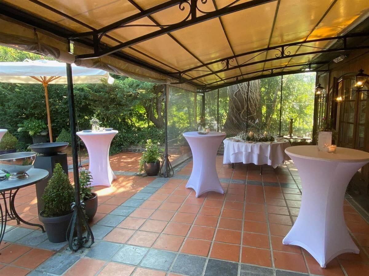 Eine Terrasse mit Tischen und Sonnenschirmen unter einem Baldachin.