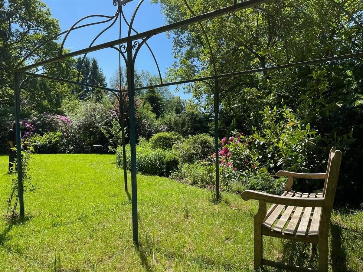 Eine Holzbank steht unter einem Pavillon in einem Garten.
