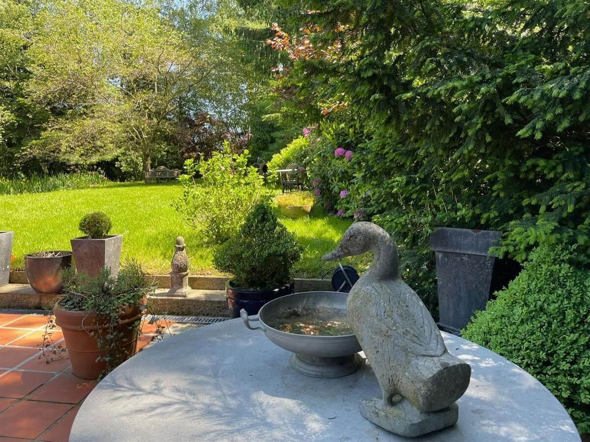 Eine Entenstatue sitzt auf einem Tisch neben einem Vogelbad.