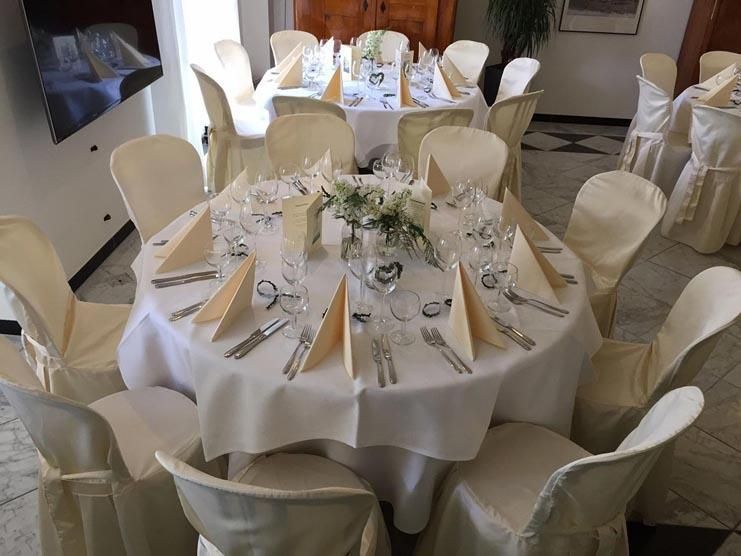 Ein runder Tisch mit einer weißen Tischdecke und weißen Stühlen ist für einen Hochzeitsempfang gedeckt.