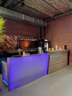 Eine Bar mit violettem Licht in einem Raum mit einer Ziegelwand.