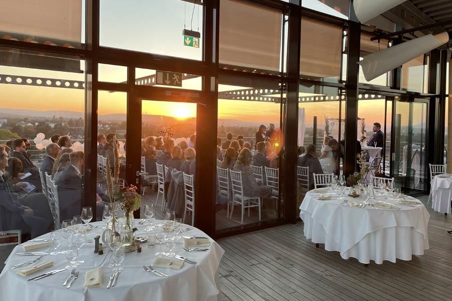 Eine Gruppe von Menschen sitzt in einem Raum an Tischen und blickt auf den Sonnenuntergang.