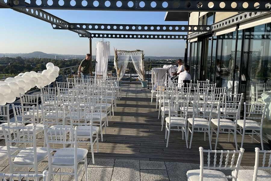 Auf einer Terrasse steht eine Reihe weißer Stühle.