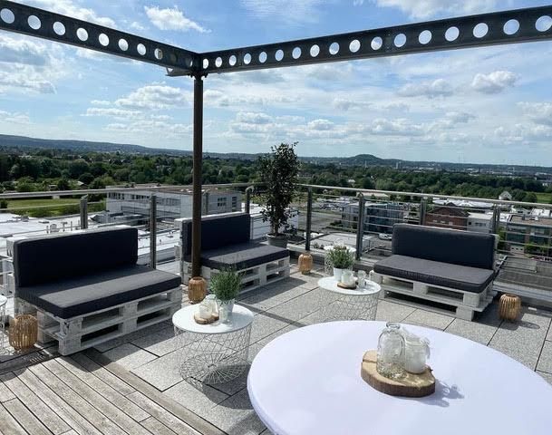 Eine Dachterrasse mit Blick auf die Stadt und einer Couch aus Paletten.
