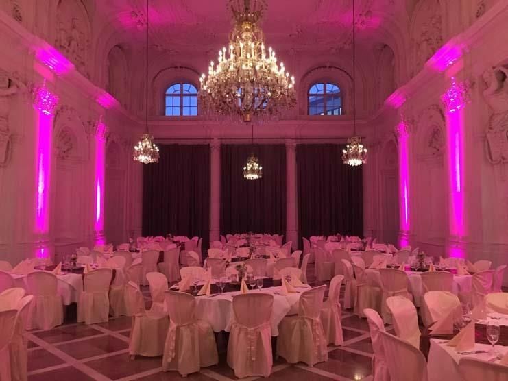 Ein großer Raum mit rosa Lichtern an den Wänden und Tischen und Stühlen
