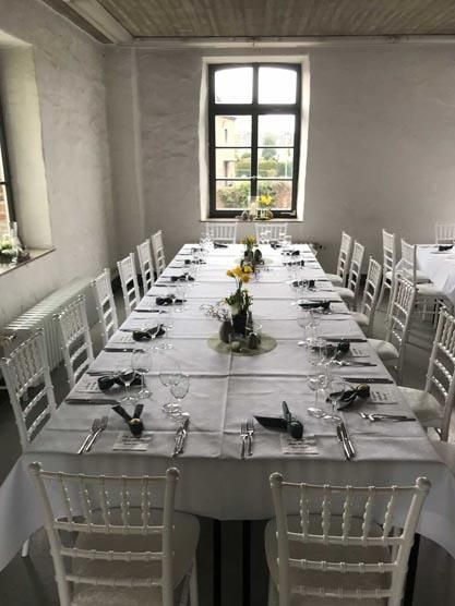 Ein langer Tisch mit weißen Tischen und Stühlen in einem Raum mit einem Fenster.