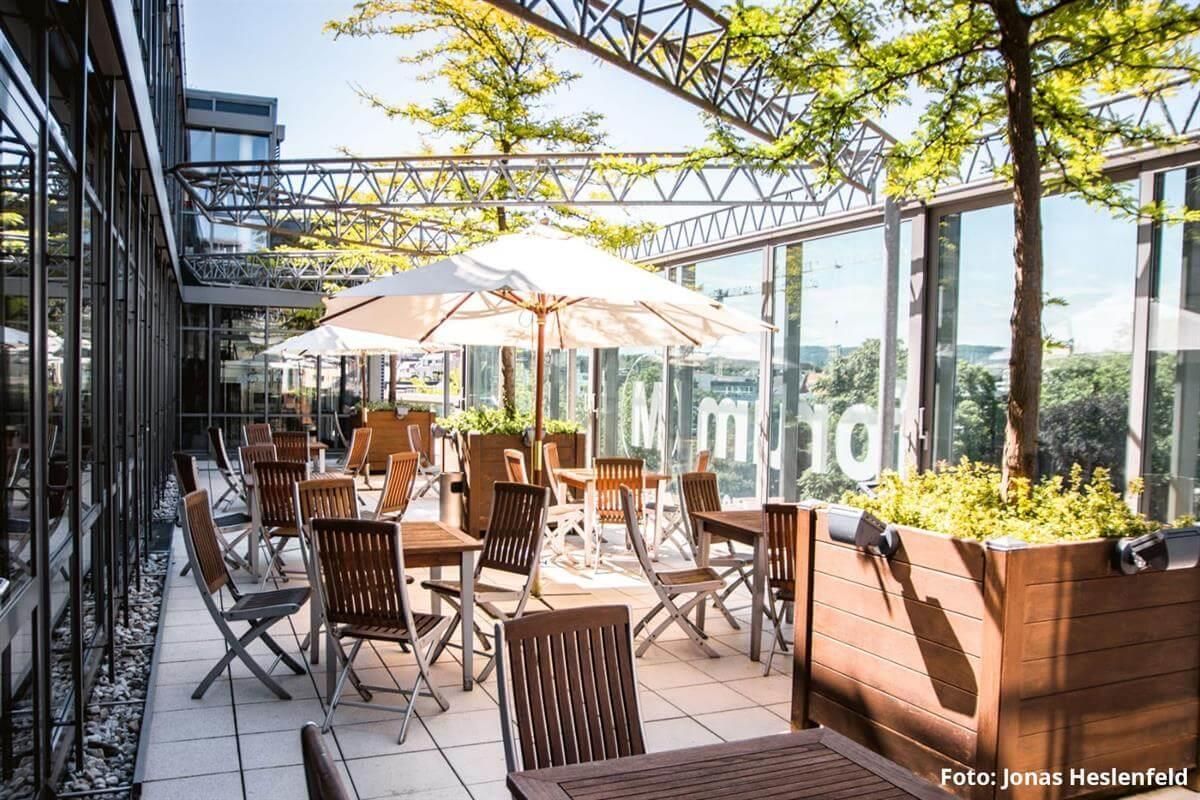 Eine Terrasse mit Tischen, Stühlen und Sonnenschirmen vor einem Gebäude.