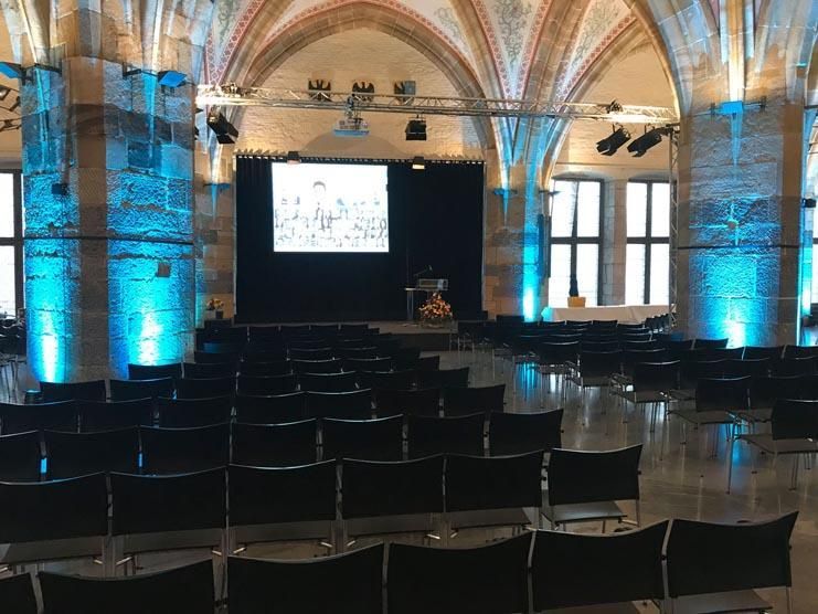 Ein großer Raum mit Stuhlreihen und einer großen Leinwand an der Wand.