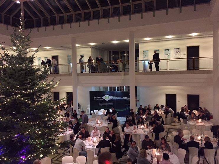 Eine Gruppe von Menschen sitzt an Tischen mit einem Weihnachtsbaum im Hintergrund