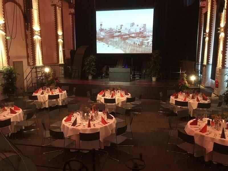 Ein großer Raum mit Tischen und Stühlen und einem großen Bildschirm an der Wand.