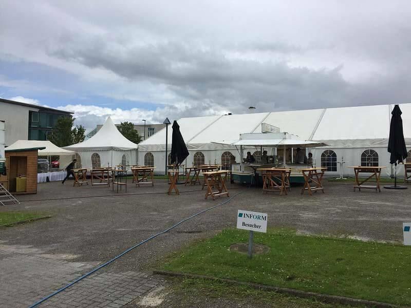 Ein großes weißes Zelt mit Tischen und Sonnenschirmen davor.