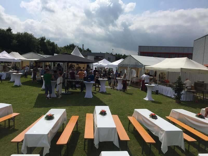 Eine Gruppe von Menschen versammelt sich auf einem Feld mit Tischen und Bänken