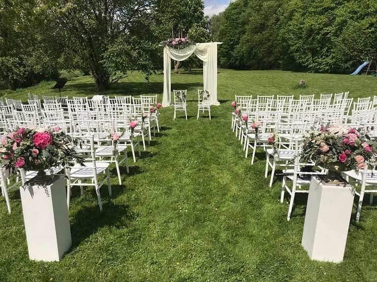 Auf einer Wiese ist eine Stuhlreihe für eine Hochzeitszeremonie aufgestellt.