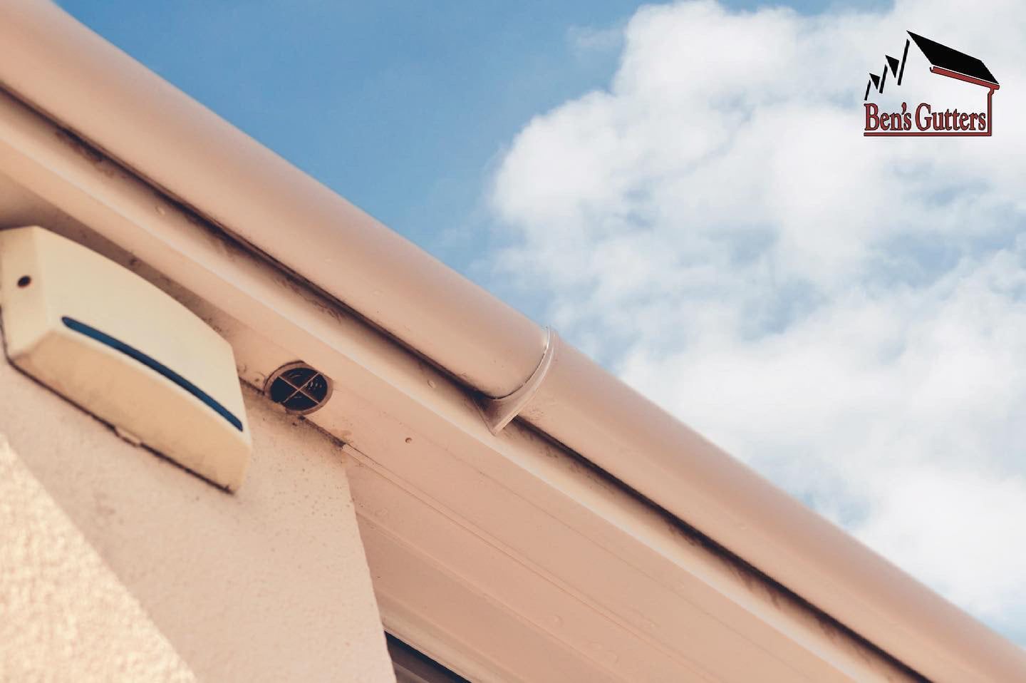 Close-up of a beige roof gutter and soffit against a cloudy blue sky