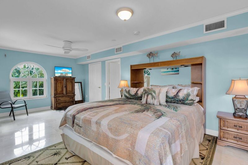 Spacious bedroom with blue walls, king bed, arched window, and wooden furniture.