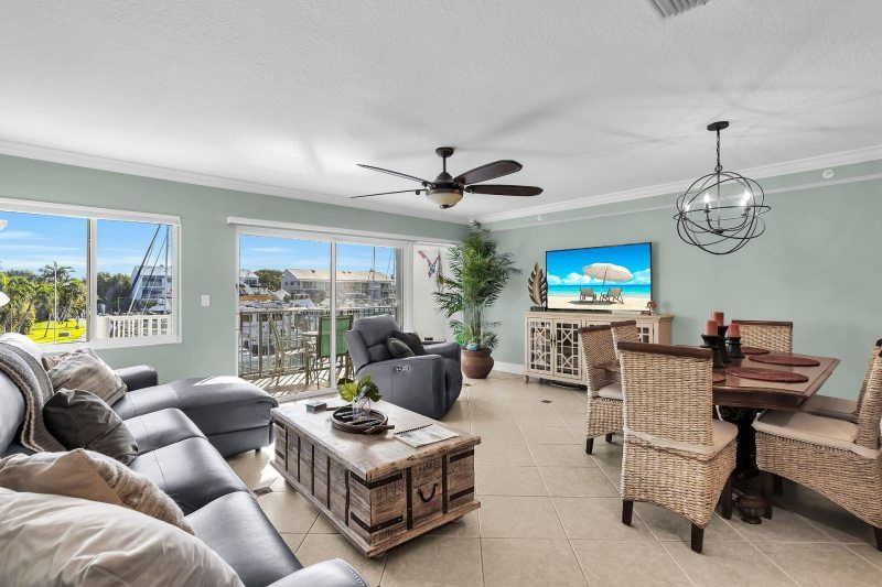 Living room with sectional sofa, TV, dining table, and balcony access. Turquoise walls, light tile floors.
