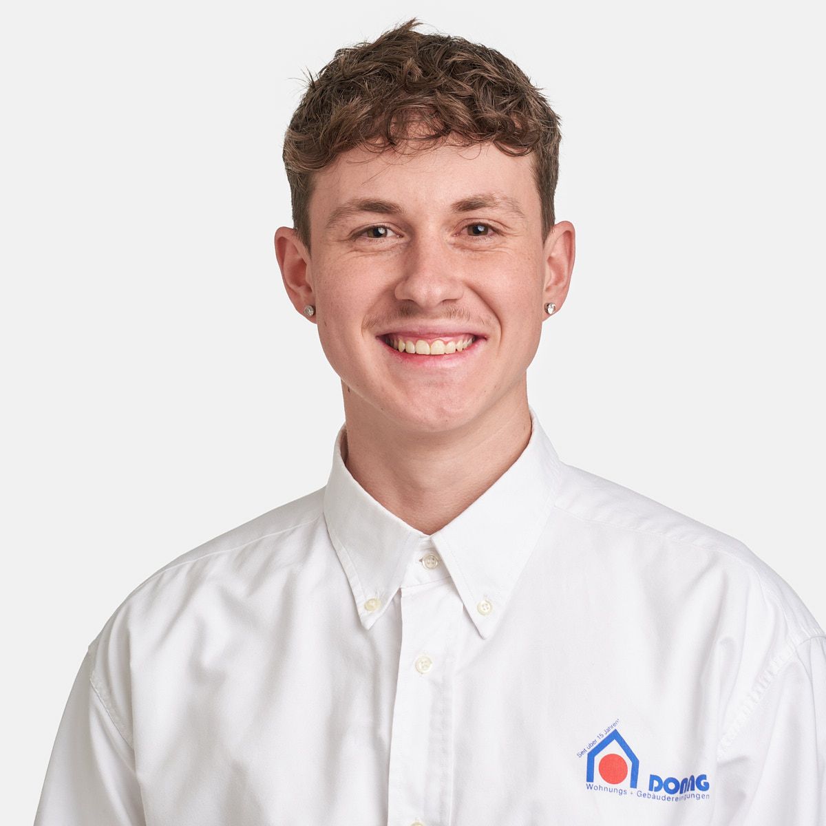 Ein Mann mit Bart trägt ein weißes Hemd und lächelt.