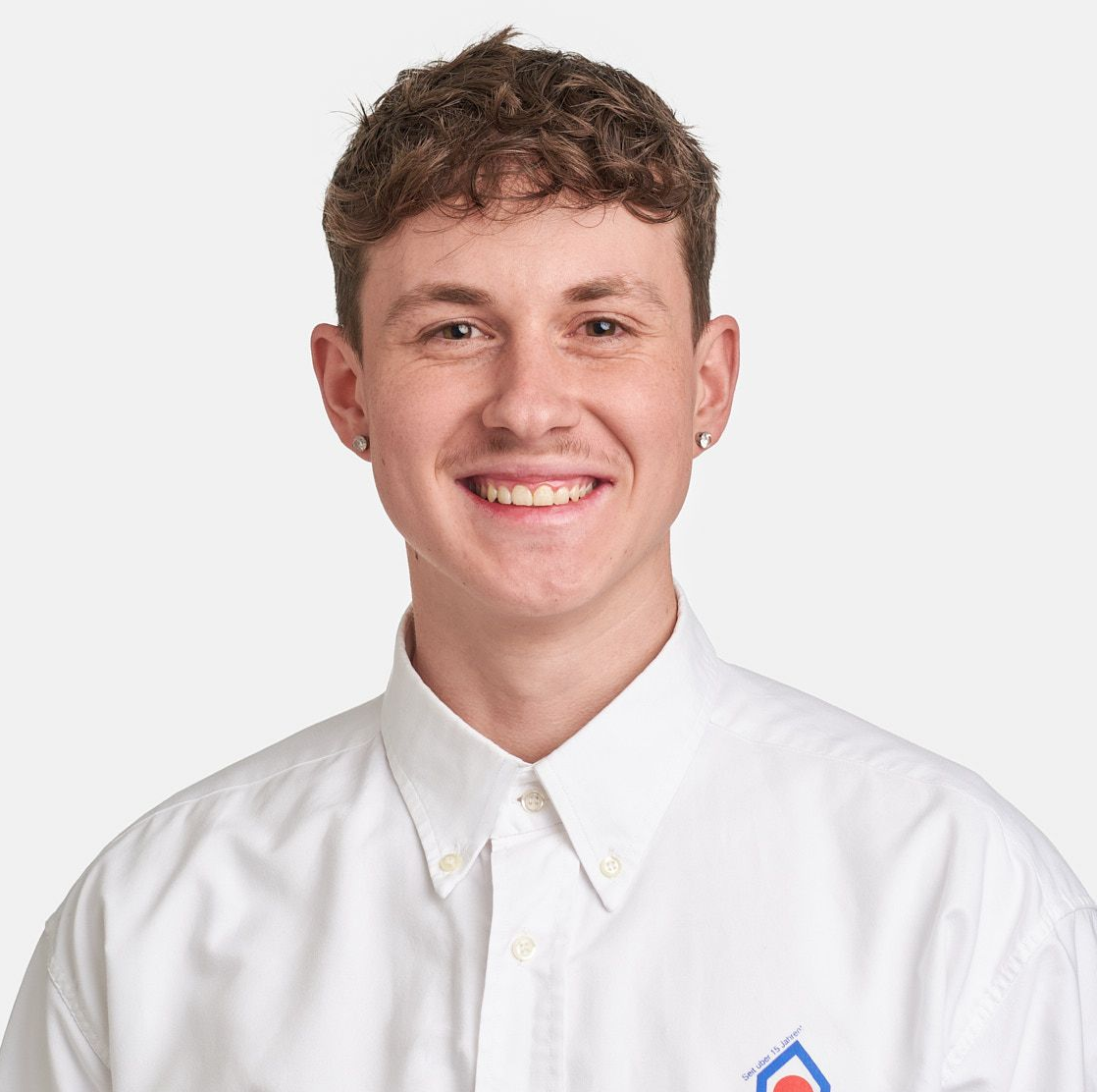 Ein Mann mit Bart trägt ein weißes Hemd und lächelt.