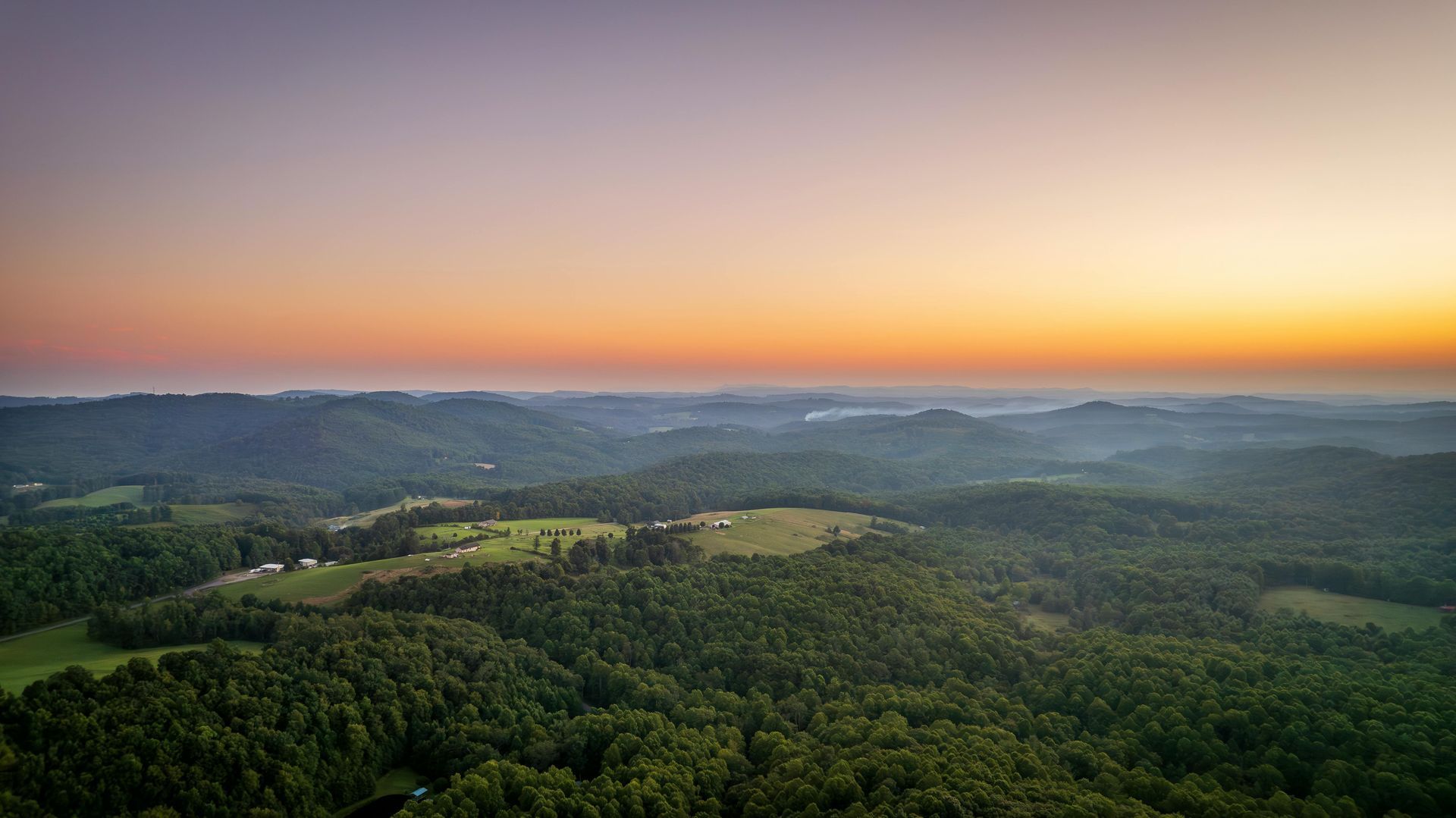 An aerial view of a sunset over a lush green forest.