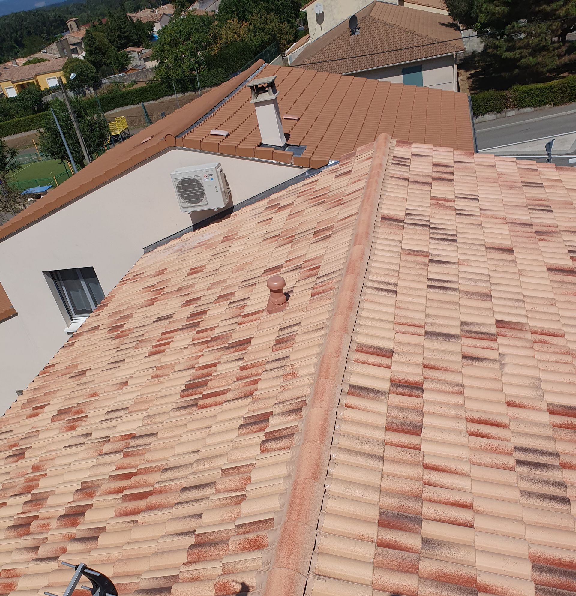Toits de tuiles en terre cuite jouxtant une maison blanche et des arbres, vus d'en haut