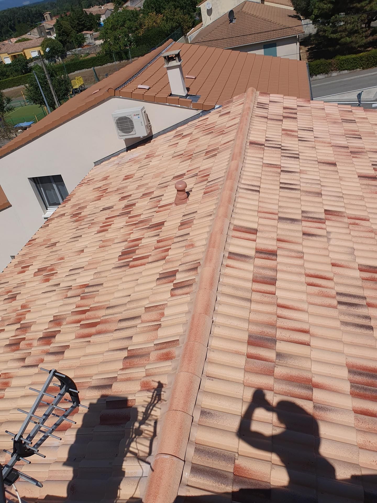 Toit avec des tuiles en terre cuite, une cheminée et l'ombre d'une personne tenant un appareil photo sur le toit