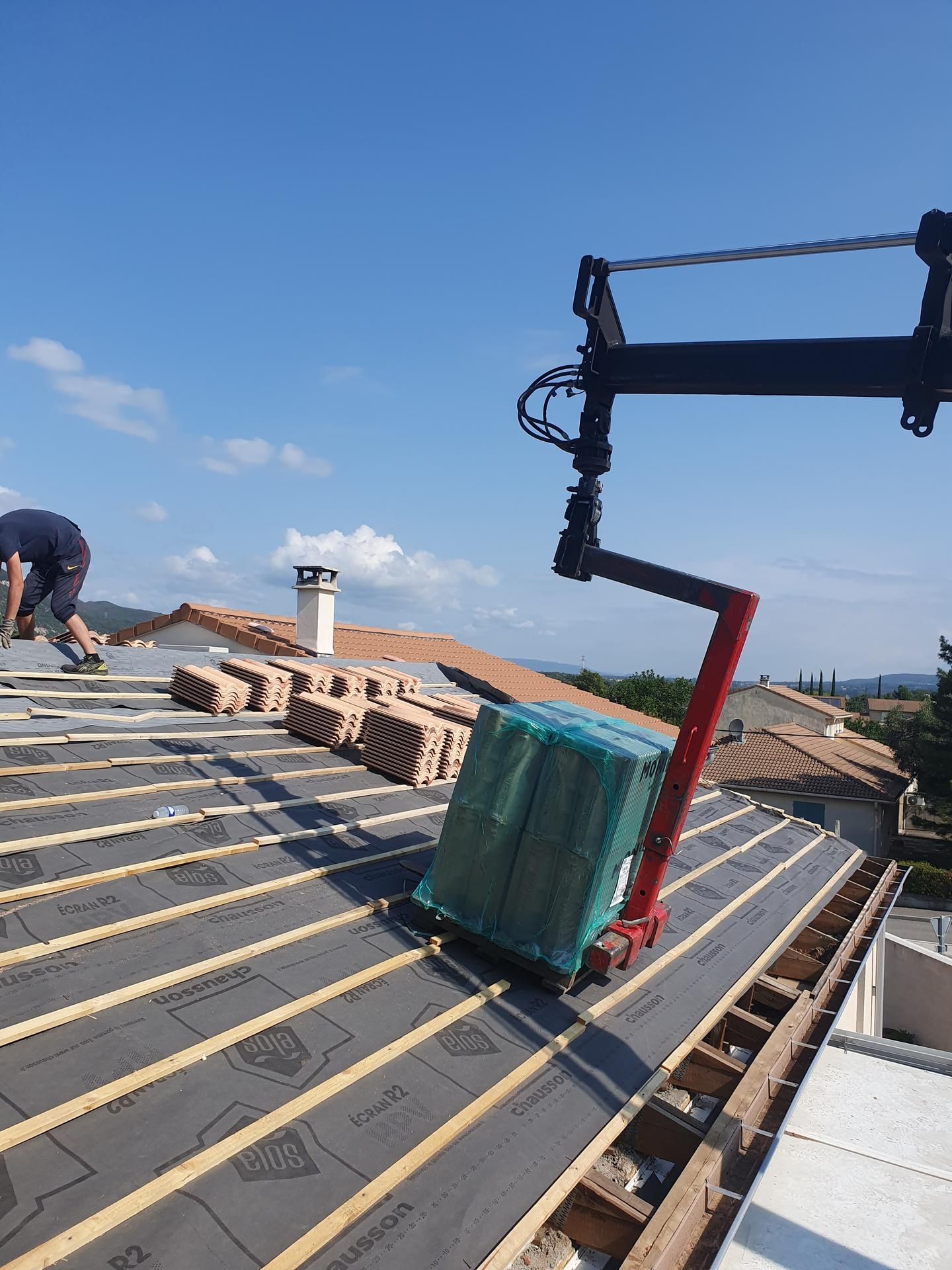 Construction sur un toit avec des briques empilées, un ouvrier et une grue sur fond de ciel bleu