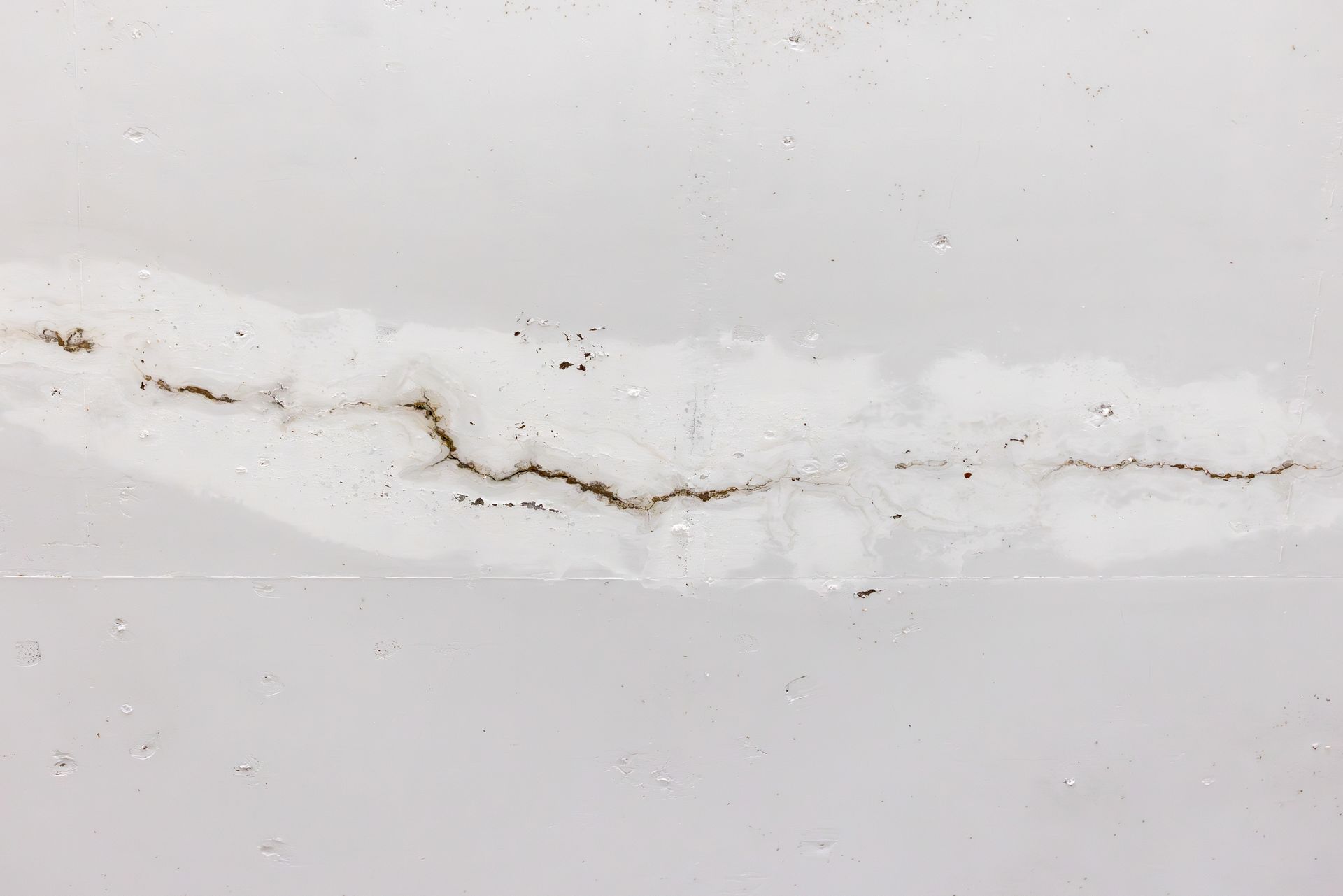 Fissure capillaire dans un mur blanc avec décoloration brune le long de la jointure