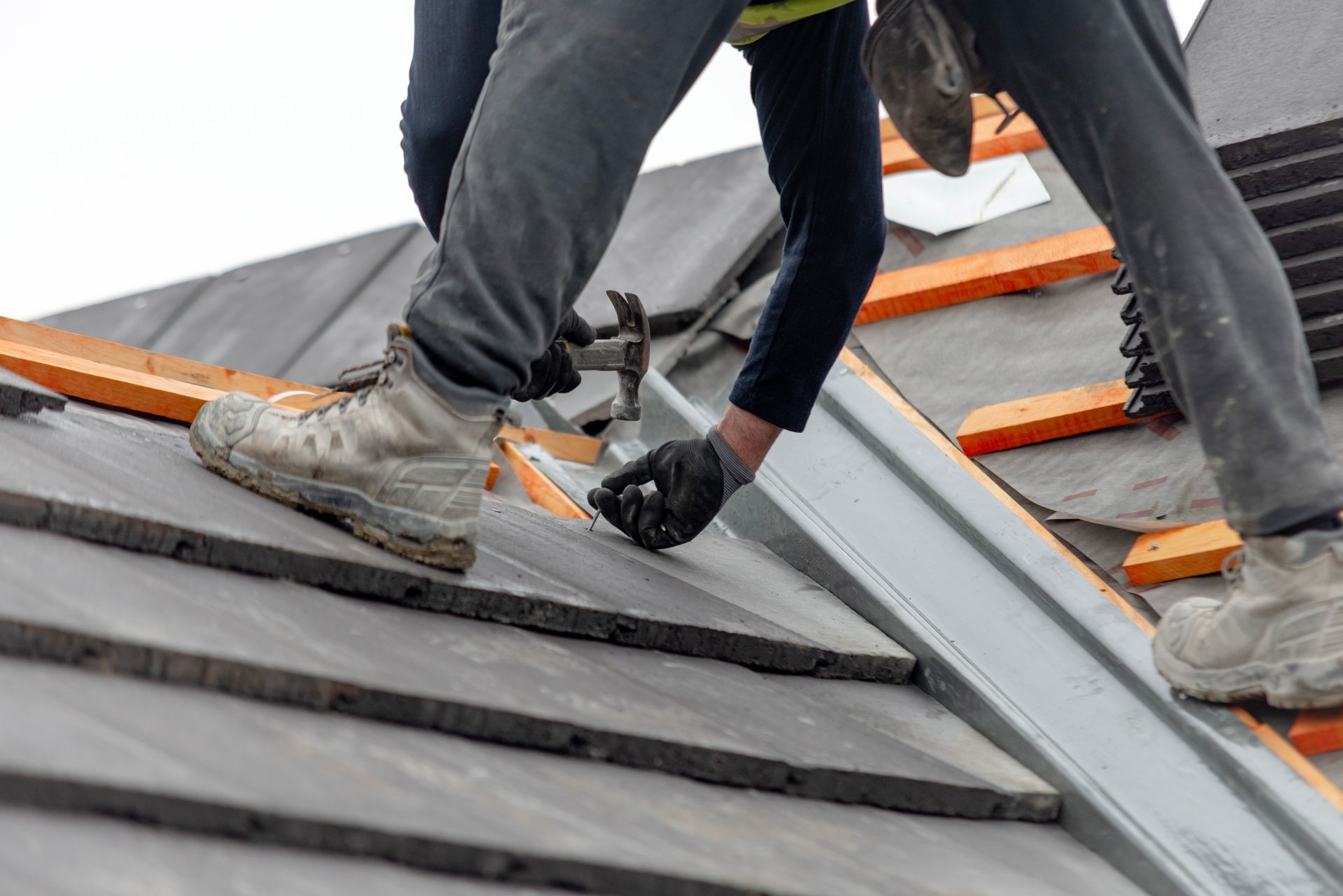 Des ouvriers installent des bardeaux sur un toit gris avec des planches de sécurité orange et une ventilation de toit en métal