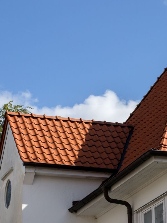 Toits de tuiles rouges et murs de maisons blanches sous un ciel bleu parsemé de quelques nuages